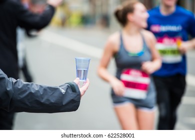 Hand Of A Volunteer Giving A Cup Of Water At A Refreshment Point In A Marathon Race To Runners.