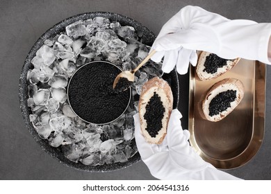 hand of waiter in gloves take a black caviar in spoon for bread with butter