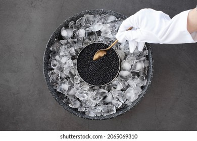hand of waiter in white gloves take a black caviar in spoon