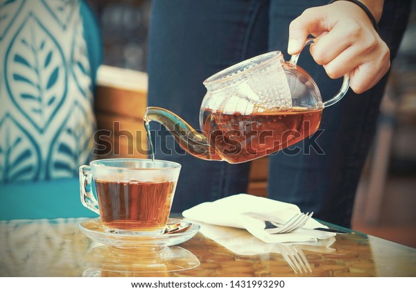 ウェイトレスの手が客のテーブルに紅茶を注ぐ お茶を入れたグラスティーポットの接写 ウエイトレスはホテルの客に茶を注ぐ 調色 の写真素材 今すぐ編集
