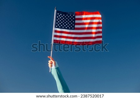 
Hand Waiving an American Flag on a Blue Sky. Cheerful enthusiastic patriotic person displaying the symbol of the USA
