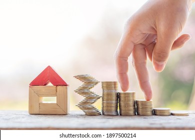 Hand walking on coin stack and house model resting on wooden desk - Shutterstock ID 1897500214