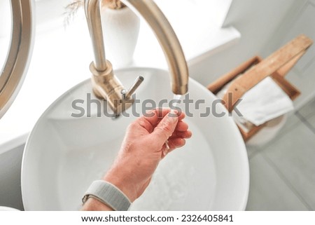 Hand washing with faucet over the washbasin in modern bathroom. Rotary nozzle on the mixer to adjust the flow of water. White bathroom sink for washing hands