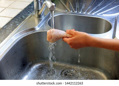 A Hand Washing A Raw Chicken Leg Under Water In The Kitchen Sink. Splashing Water From The Chicken Can Cause Bacteria To Be Spread On To Work Surfaces And Cooking Equipment.