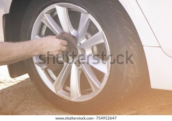 Hand washing the tire , wheel of the car.\
A man\
cleaning from dust and dirt a new brand sport car modern sedan with\
a rag , a silver rim tyre.A concept of taking care of personal\
car,loving gear.