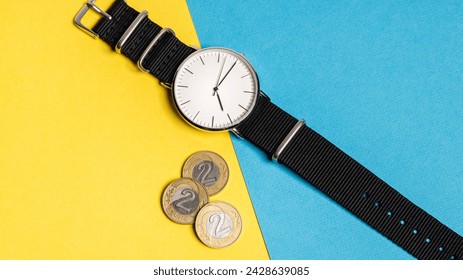 A hand watch with a white shield and tips lying on a yellow-blue background. Next to the Polish coins of PLN. Photo concept