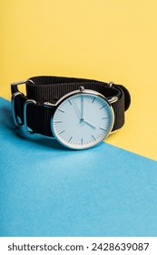 A hand watch with a white shield and tips lying on a yellow-blue background. Photo concept