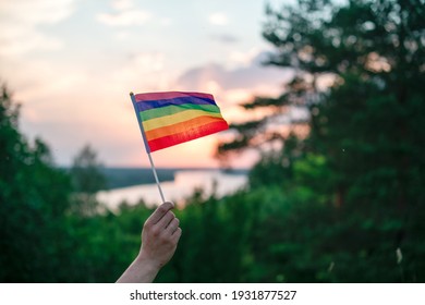 Una mano arroja una colorida bandera arcoíris LGBT de orgullo gay al atardecer en un paisaje natural en verano