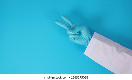 Hand Wear Blue Latex Glove And Arm Wear Doctor Gown Is Doing Victory Hand Or Peace Sign On Blue Background.