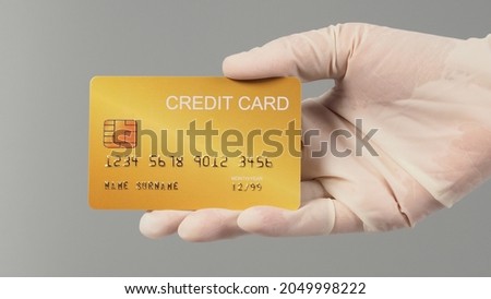 Hand is wear medical glove and holding gold credit card isolated on grey background.