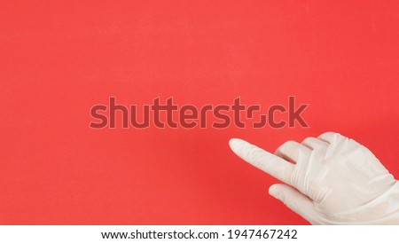 Hand wear white medical glove and point the finger on red background.