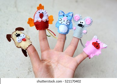 Hand wearing 5 finger puppets: dog, cock, cat, mouse, pig