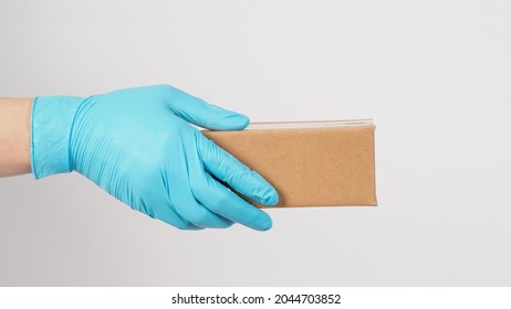 Hand Wearing Blue Latex Glove And Holding Brown Box Isolated On White Background.