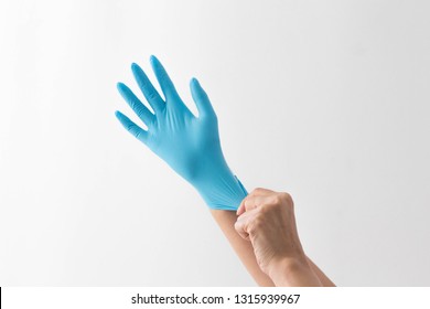 A Hand Wearing A Blue Medical Glove With Another Hand Holding It In Isolated White Background