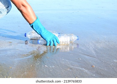 A Hand Wearing Blue Rubber Gloves Is Picking Up A Clear Plastic Empty Water Bottle On Beach Concept Garbage On The Beach