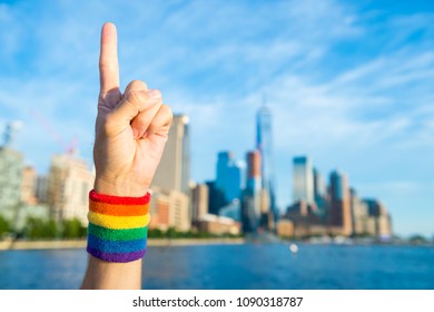 Hand Wearing Gay Pride Rainbow Sweat Band Making 'number One' Hand Sign In Front Of City Skyline