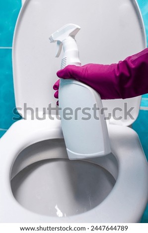 A hand wearing a pink glove carefully pours toilet cleaner from a bottle into the open toilet bowl, ensuring thorough cleaning.