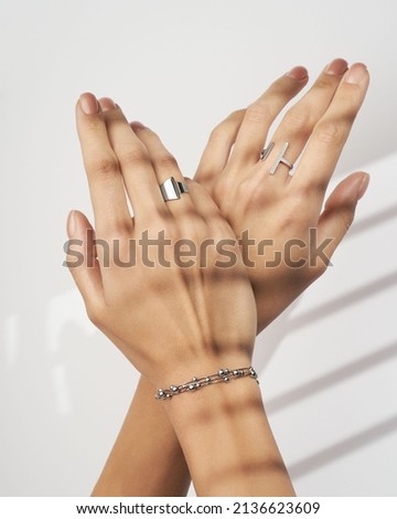 Hand wearing silvers jewelry bracelet and rings on soft white background. Still life and creative photo with shadows.
