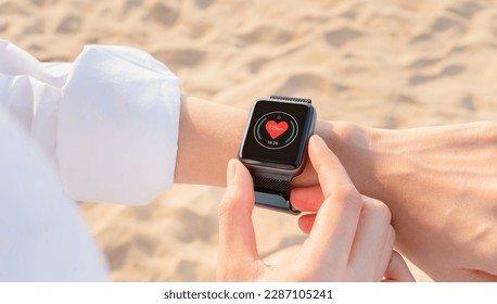 Hand wearing a smartwatch and checking active lifestyle and using fitness tracker outdoor on the beach. - Powered by Shutterstock