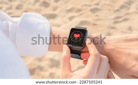 Hand wearing a smartwatch and checking active lifestyle and using fitness tracker outdoor on the beach.