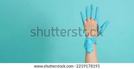 Hand Wearing torn medical gloves or torn rubber gloves on blue or mint green background.monotone coclor.