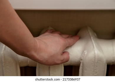 Hand Of A White European Woman Touches The Old Iron Central Heating Radiator.