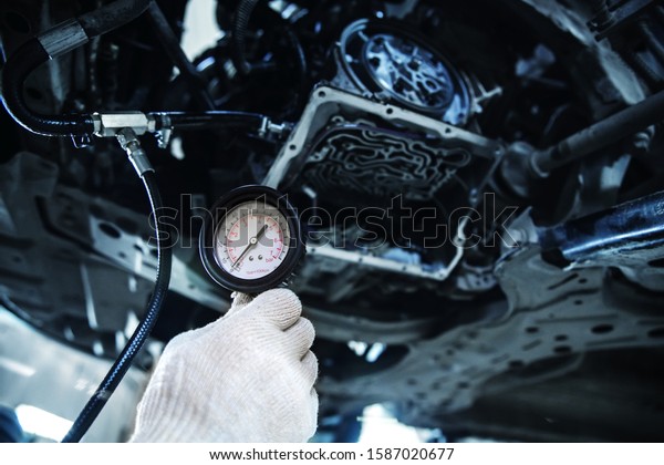 hand in a white glove holds a manometer against the\
background of a partially dismantled automatic transmission with a\
shallow depth of field