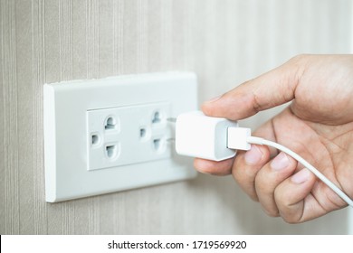 Hand And White Plug In Electric Socket On Wall.