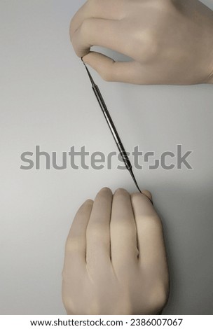 A hand in a white sterile medical glove holds a metal instrument.