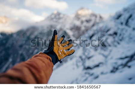 Hand winter sport glove on snow, ice and rock in the background. Snow and ice, blue sky. Winter climbing, hiking and ski touring. Point of view of an climbing tool in a hand of an alpinist.