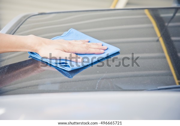 Hand\
wipe cleaning the car with blue microfiber\
cloth