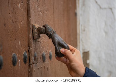 Hand Of A Woman Catching An Antique Hand Shaped Knocker With A Ball On A Wooden Door With Large Iron Nails