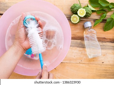 hand of woman cleaning milk bottles of baby with cleanser liquid washing extract from herbal kaffir lime on background wooden