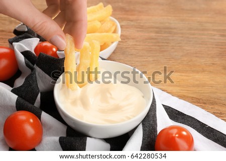 Hand of woman eating French fries with tasty mayonnaise sauce, closeup