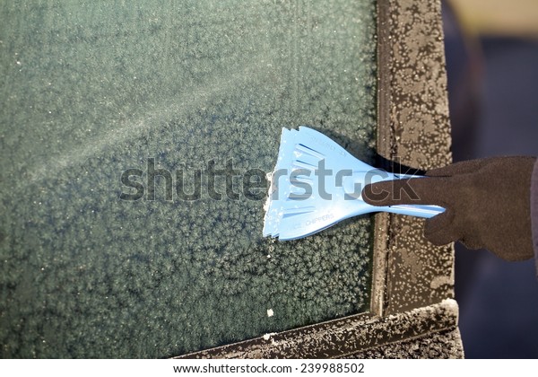 Hand of woman in glove scraping ice and snow\
from car windscreen