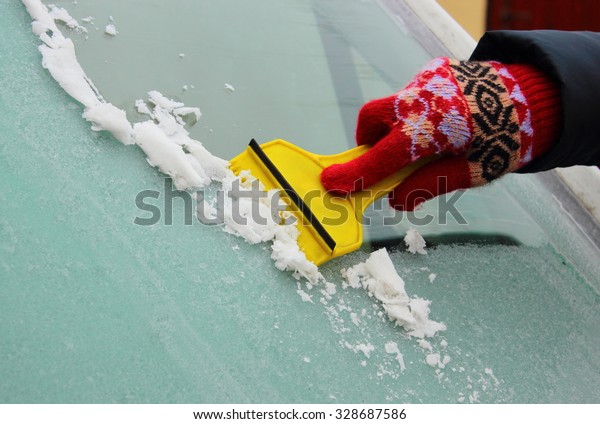 Hand of woman in glove scraping ice and snow\
from car windscreen