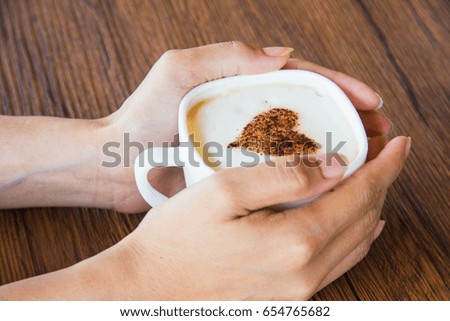 hand of woman with heart on latte art coffee on wooden table with vintage tone. Soft focus