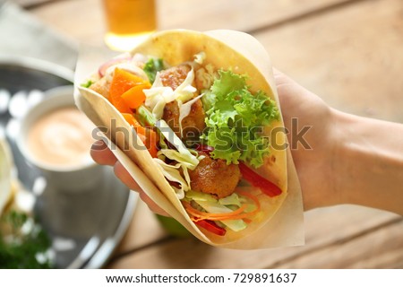 Hand of woman holding delicious fish taco, closeup