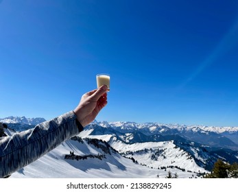 Hand Of Woman Holding Glass Of Eggnog Against Spectacular Winter Panorama In The Austrian Alps. Vorarlberg, Austria. High Quality Photo