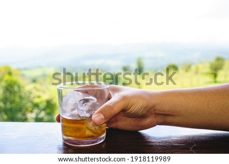 Hand of a woman holding a glass of michelada with a forest landscape in the background