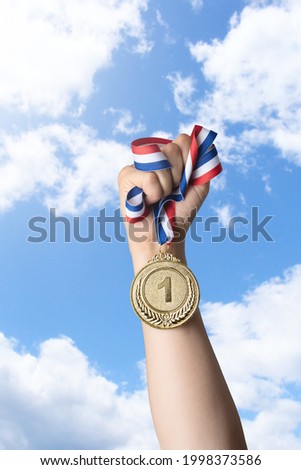 Hand of woman holding gold medal against sky.award and victory concept.copy space