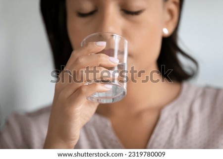 Hand of woman holding transparent glass of pure water at mouth, drinking with closed eyes, feeling thirsty, unwell, tired, taking pills. Healthy metabolism, diet, dehydration concept. Close up