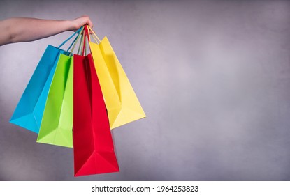 Hand of a woman holds two shopping bags  in blue, green, red and yellow. On the right is space to put in your own text.