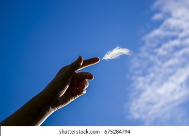 Hand Of A Woman Letting Go A White Feather On Blue Sky Background And Some Clouds