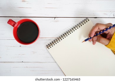 Hand of woman in mustard yellow sweater holding polka dot pencil to write some text or messages on blank white writing paper space e.g. Merry Christmas, New Year’s Resolutions, To Do or Wish List 2019