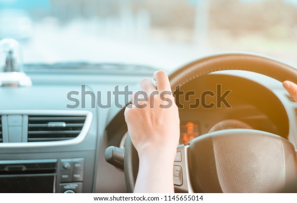 Hand of woman on steering wheel drive a car\
with sunlight background.