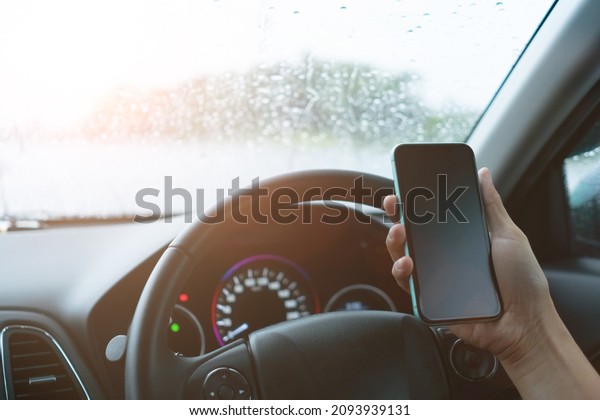 Hand of woman on steering wheel\
drive a car while using smartphone sunlight\
background.