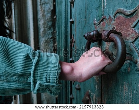 the hand of a woman opening an old green wooden door of the cathedral of girona