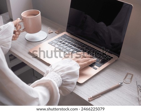 Hand of a woman operating a computer while drinking a drink at a wooden desk, a woman working at a cafe       