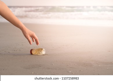 The Hand Of A Woman Is Picking Up A Plastic Bottle To Clean The Beach.